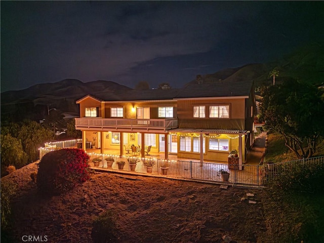 back of house at twilight with a patio, a balcony, and fence