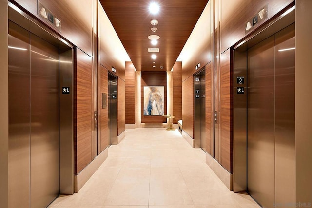 hall featuring light tile patterned floors, wooden walls, a package area, and elevator