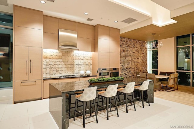 kitchen with a breakfast bar area, backsplash, stainless steel appliances, light tile patterned flooring, and exhaust hood