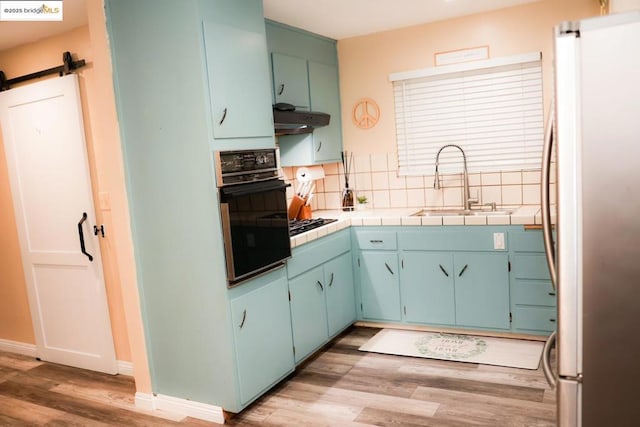 kitchen with sink, stainless steel fridge, oven, tile counters, and a barn door