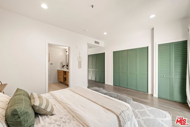 bedroom featuring connected bathroom, light hardwood / wood-style flooring, and multiple closets