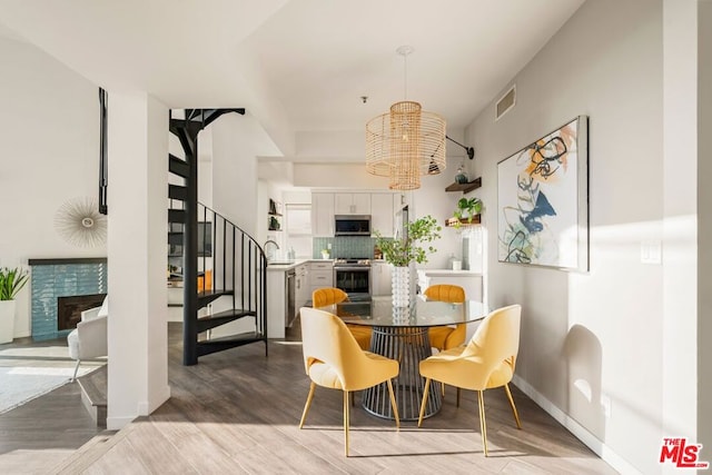 dining room featuring a tiled fireplace, sink, a chandelier, and light hardwood / wood-style flooring