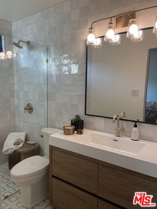 bathroom with tile walls, vanity, tile patterned floors, and a tile shower