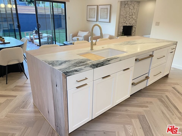 kitchen with sink, light stone countertops, white cabinets, a center island with sink, and light parquet flooring