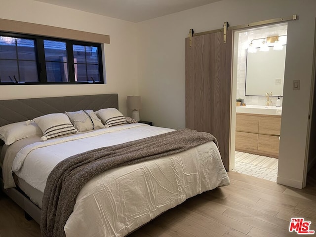 bedroom with hardwood / wood-style floors, sink, ensuite bath, and a barn door