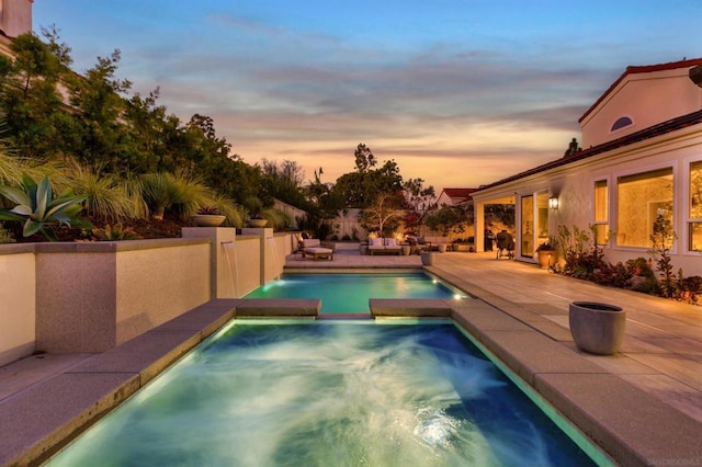 pool at dusk featuring an in ground hot tub and a patio area