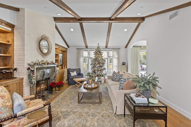 living room with lofted ceiling with beams, wood-type flooring, and a fireplace