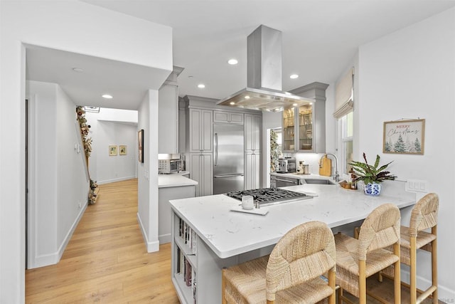 kitchen featuring gray cabinets, appliances with stainless steel finishes, island range hood, sink, and kitchen peninsula