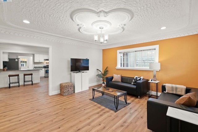 living room with a textured ceiling, ornamental molding, a chandelier, and light wood-type flooring