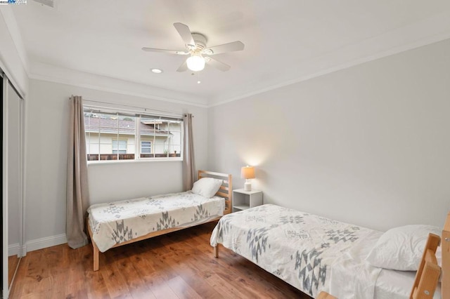 bedroom featuring wood-type flooring, ornamental molding, ceiling fan, and a closet