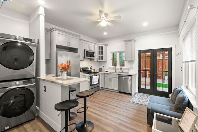 kitchen featuring appliances with stainless steel finishes, french doors, stacked washer and clothes dryer, light stone countertops, and light hardwood / wood-style flooring