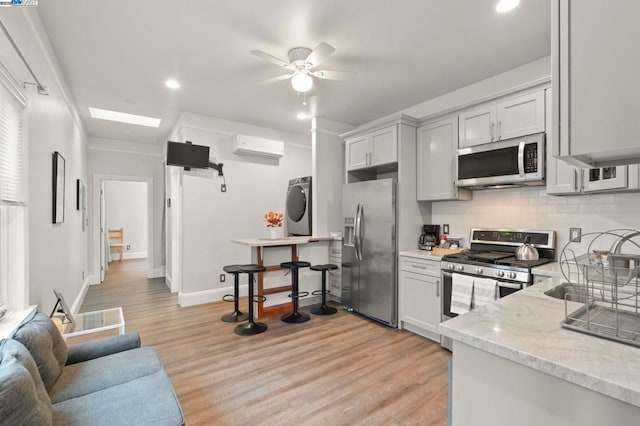 kitchen with appliances with stainless steel finishes, a wall unit AC, washer / clothes dryer, light hardwood / wood-style floors, and decorative backsplash