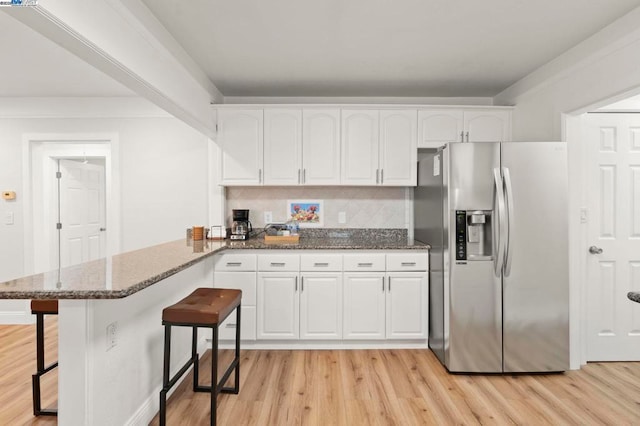 kitchen featuring a breakfast bar, stainless steel fridge with ice dispenser, kitchen peninsula, dark stone counters, and white cabinets