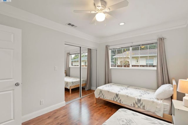 bedroom with wood-type flooring, ornamental molding, ceiling fan, and a closet