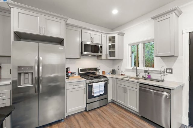 kitchen featuring appliances with stainless steel finishes, sink, decorative backsplash, hardwood / wood-style flooring, and light stone countertops