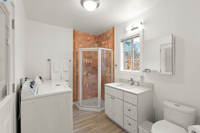 bathroom featuring washer and dryer, a shower with shower door, hardwood / wood-style flooring, vanity, and toilet