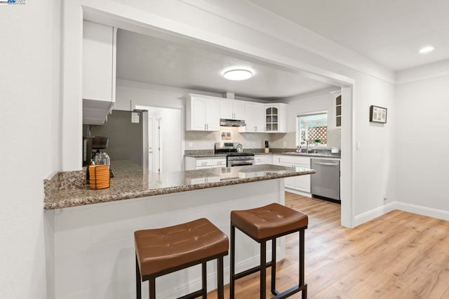 kitchen featuring dark stone counters, kitchen peninsula, white cabinets, and appliances with stainless steel finishes