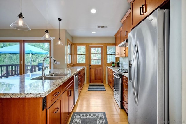 kitchen featuring sink, stainless steel appliances, hanging light fixtures, and an island with sink