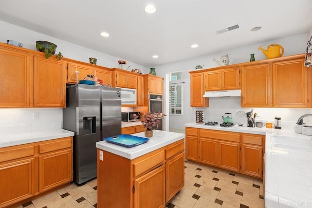 kitchen with visible vents, under cabinet range hood, tile countertops, stainless steel appliances, and a sink