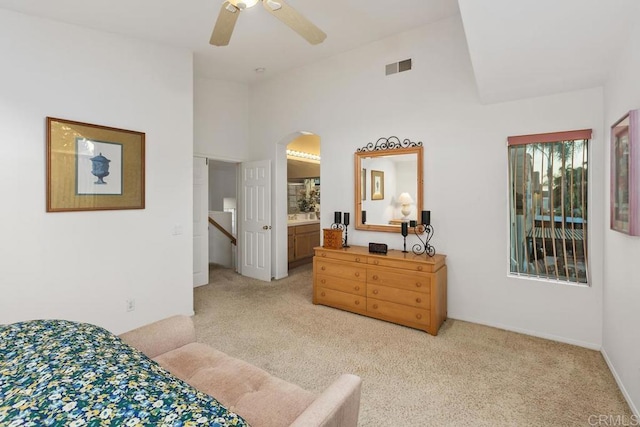 bedroom featuring visible vents, vaulted ceiling, light carpet, ensuite bathroom, and arched walkways