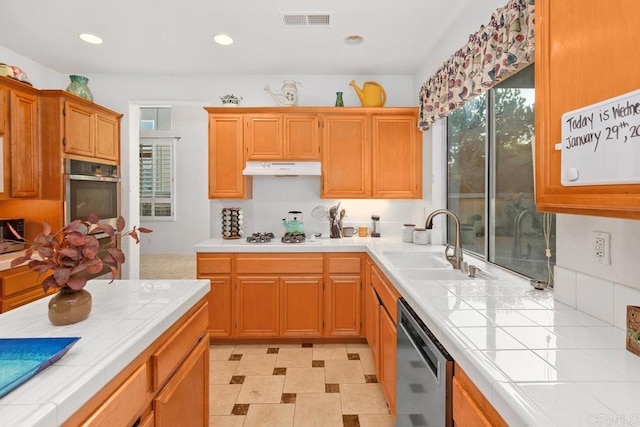 kitchen with tile countertops, visible vents, a sink, under cabinet range hood, and appliances with stainless steel finishes