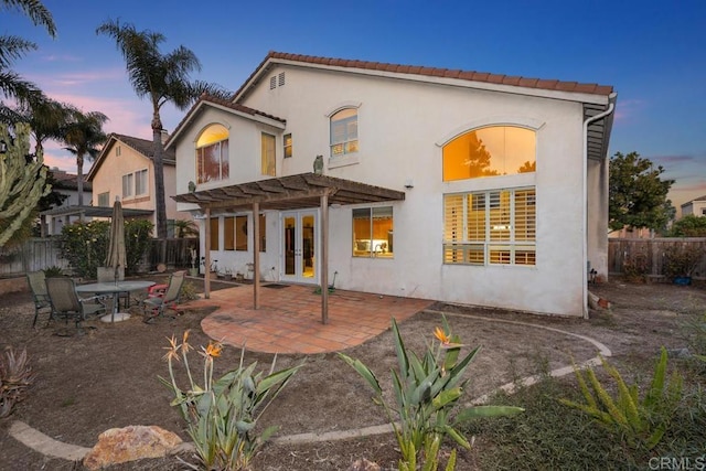 back of property at dusk with a patio, fence, a pergola, stucco siding, and french doors