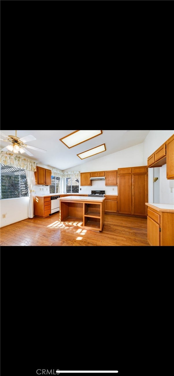 kitchen featuring ceiling fan, dishwasher, vaulted ceiling with skylight, wall chimney exhaust hood, and light wood-type flooring