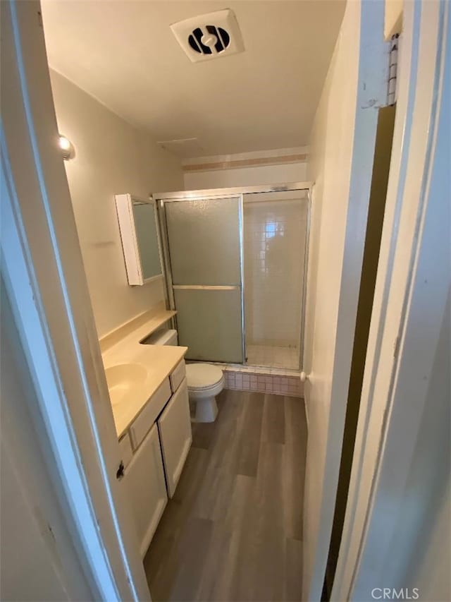 bathroom featuring toilet, wood finished floors, visible vents, vanity, and a shower stall