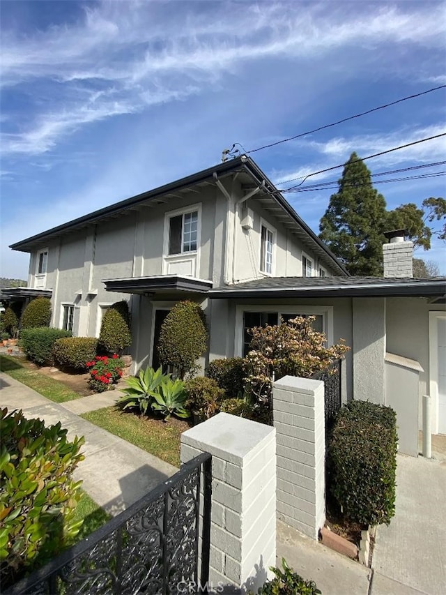 view of side of property featuring a chimney, fence, and stucco siding