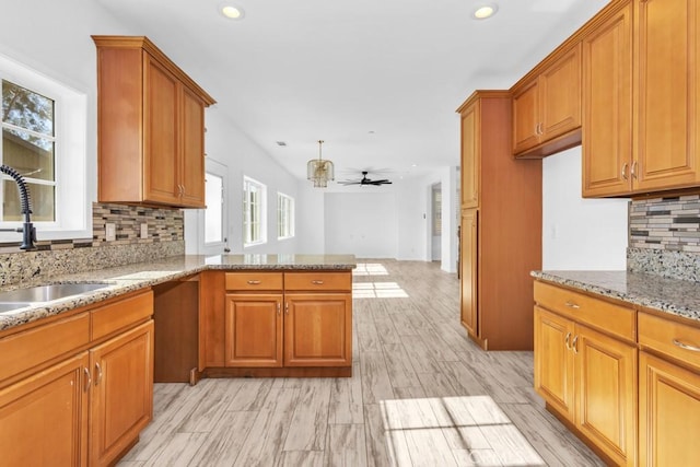 kitchen featuring kitchen peninsula, sink, backsplash, ceiling fan, and light stone counters