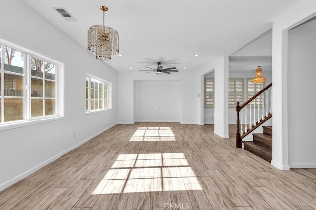 unfurnished living room featuring ceiling fan with notable chandelier and light hardwood / wood-style flooring