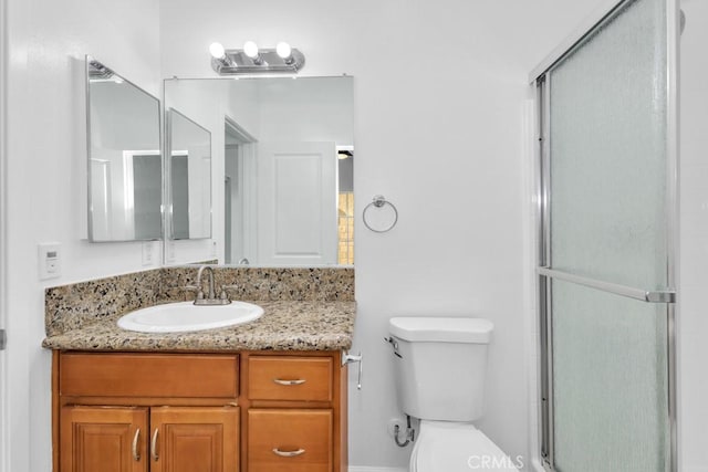 bathroom with a shower with door, vanity, and toilet