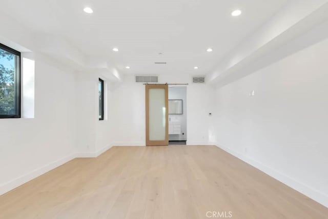 unfurnished room featuring a barn door, a wealth of natural light, and light wood-type flooring