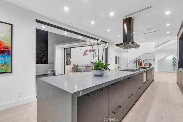 kitchen featuring a spacious island, light stone counters, light wood-type flooring, island exhaust hood, and stainless steel gas stovetop