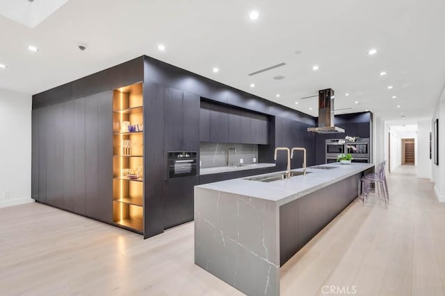 kitchen featuring a large island with sink, island exhaust hood, sink, and light hardwood / wood-style flooring