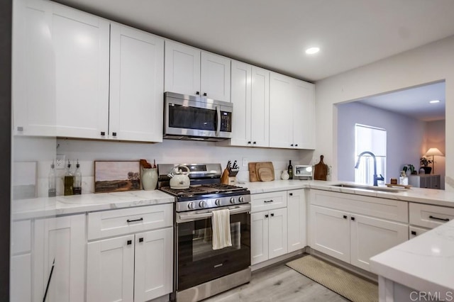 kitchen with stainless steel appliances, white cabinetry, sink, and light stone counters