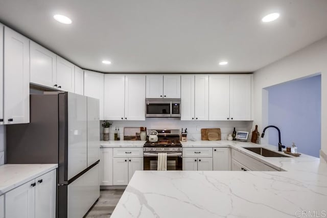 kitchen featuring sink, light stone counters, light hardwood / wood-style flooring, stainless steel appliances, and white cabinets