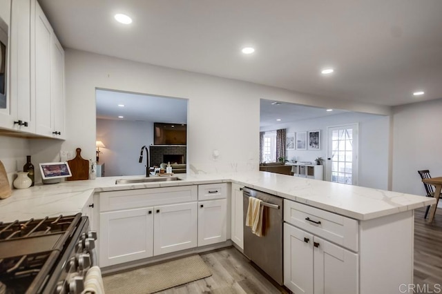 kitchen with sink, white cabinetry, stainless steel appliances, light hardwood / wood-style floors, and kitchen peninsula