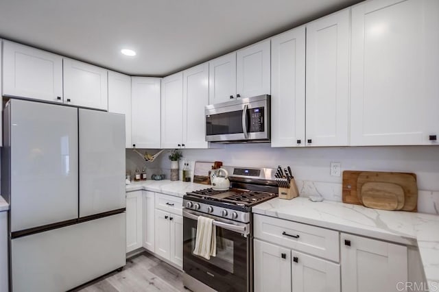 kitchen with stainless steel appliances, white cabinetry, light stone counters, and light hardwood / wood-style flooring