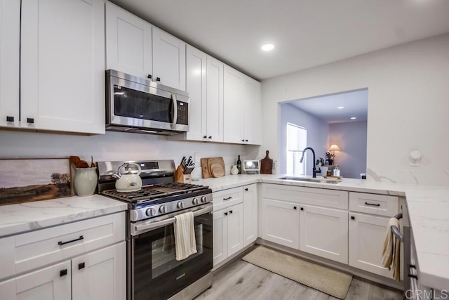 kitchen with sink, white cabinetry, light wood-type flooring, stainless steel appliances, and light stone countertops