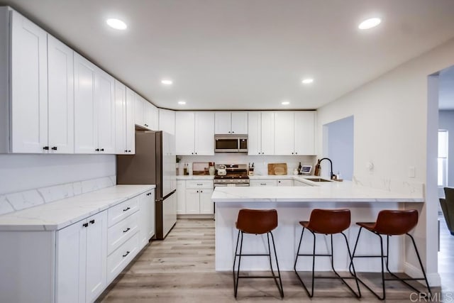 kitchen featuring appliances with stainless steel finishes, a breakfast bar, white cabinetry, sink, and kitchen peninsula