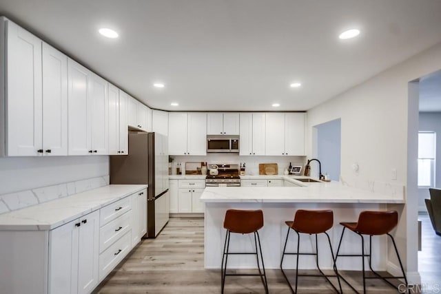 kitchen featuring a kitchen bar, sink, kitchen peninsula, stainless steel appliances, and white cabinets