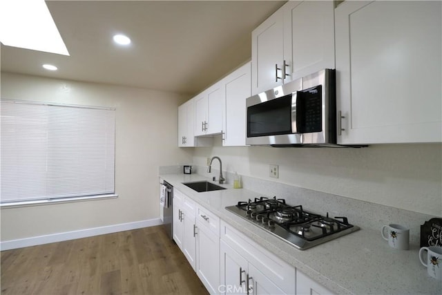 kitchen featuring sink, light stone counters, appliances with stainless steel finishes, hardwood / wood-style floors, and white cabinets