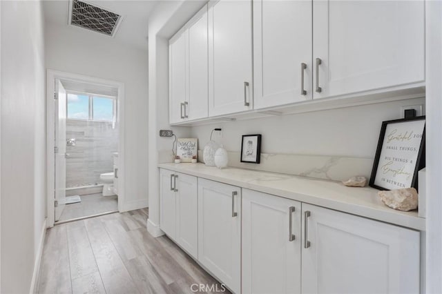 bar with light stone countertops, white cabinets, and light wood-type flooring