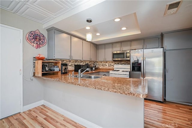 kitchen with stainless steel appliances, a tray ceiling, kitchen peninsula, and sink