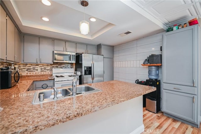 kitchen with stainless steel appliances, a tray ceiling, kitchen peninsula, and decorative light fixtures