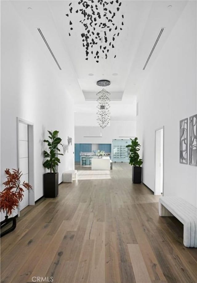 hall featuring a chandelier, wood-type flooring, a raised ceiling, and a high ceiling