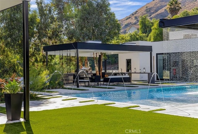 view of swimming pool with pool water feature, a mountain view, and a lawn