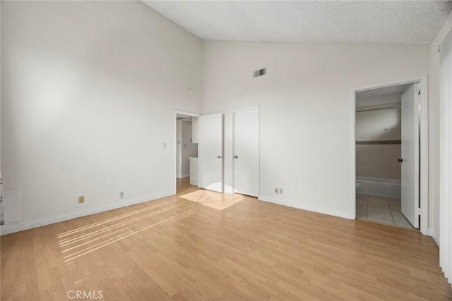 unfurnished bedroom featuring vaulted ceiling, a textured ceiling, and light wood-type flooring