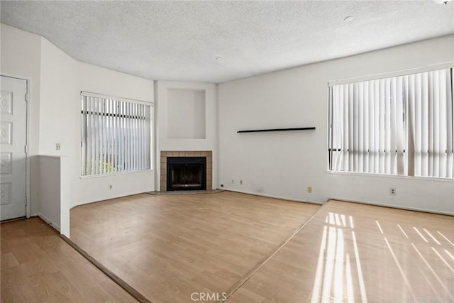 unfurnished living room featuring a tiled fireplace, a textured ceiling, and light wood-type flooring